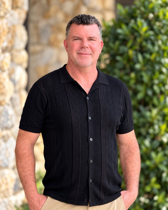 Brandon Harris, LMHC, in a black collared shirt outside his office beside stone and greenery